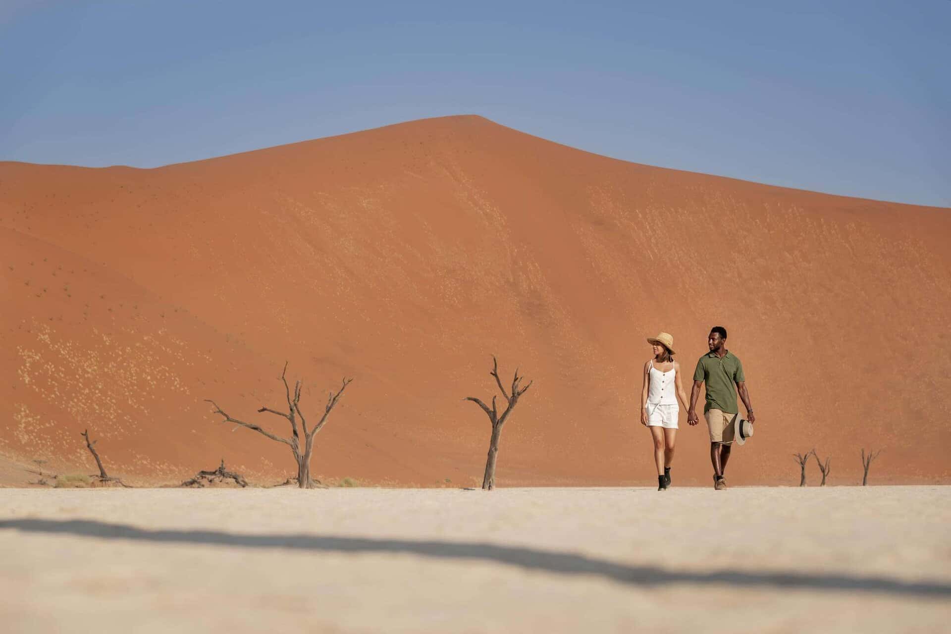 Sanddyner i Namibia med ett par som går hand i hand på en ökenexpedition.