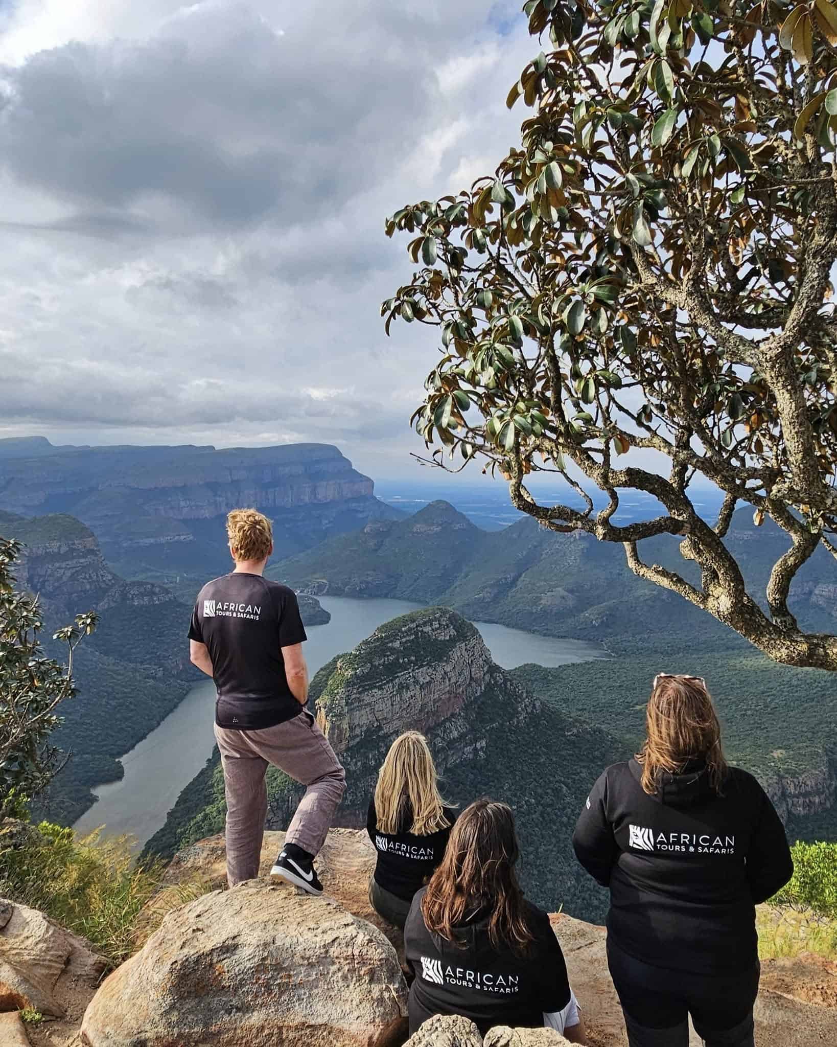 Ett safariäventyr i natursköna Afrika med turer och safaris, där en grupp i uniform står på en bergstopp och beundrar den imponerande utsikten över floder och bergskedjor, perfekt för safarientusiaster.